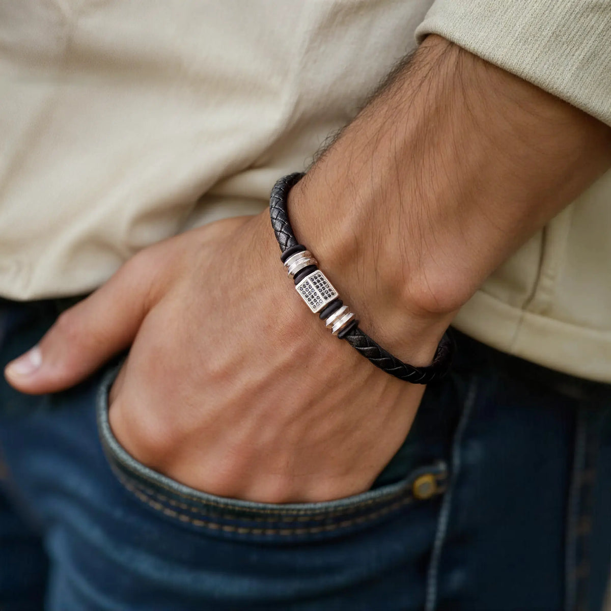 Close-up of a person wearing a black braided bracelet with a silver clasp on a wrist.