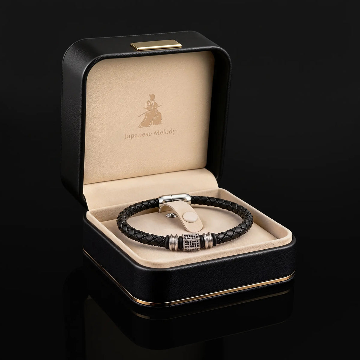 A black braided leather bracelet with silver-toned metal accents, displayed inside an open black presentation box with a beige interior. The box lid is printed with the brand name 'Japanese Melody'.