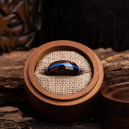 Black polished tungsten ring with blue opal and whiskey barrel oak wood. The ring is placed inside a round wooden box
