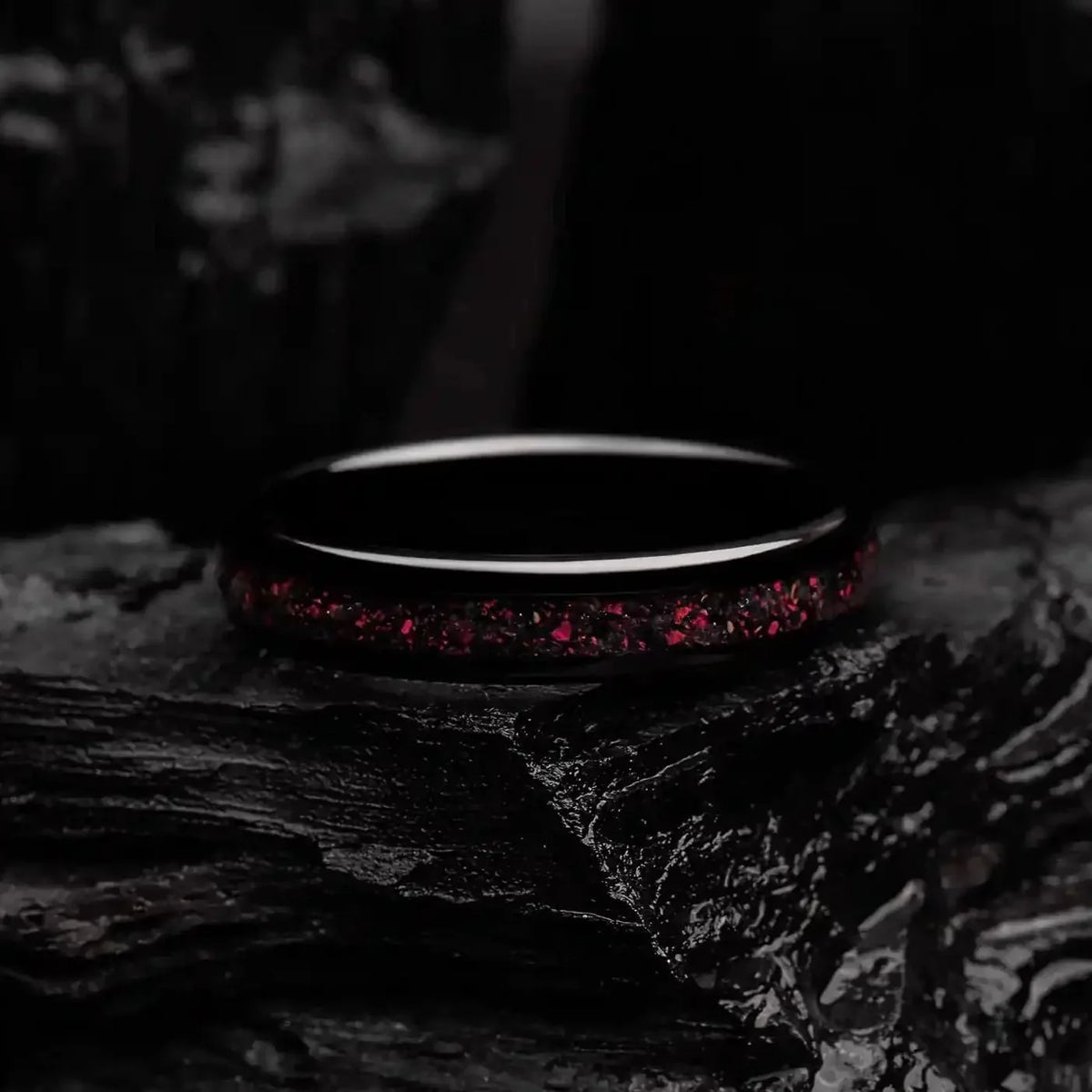 4mm black brushed tungsten ring with red opal. The ring is laying on a black coal