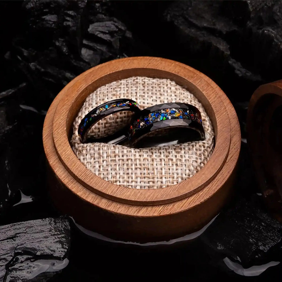 Matching wedding bands made of black hammered tungsten with galaxy opal and meteorite. The rings are placed inside a round wooden box.