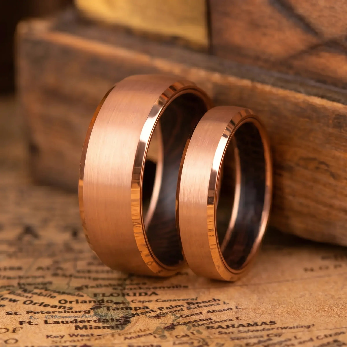 Two rose gold rings on an old map with a wooden box in the background