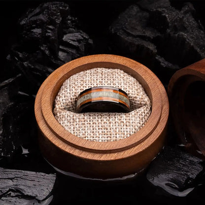 Brushed black tungsten ring with deer antler and whiskey barrel oak wood. The ring is placed inside a round wooden box.